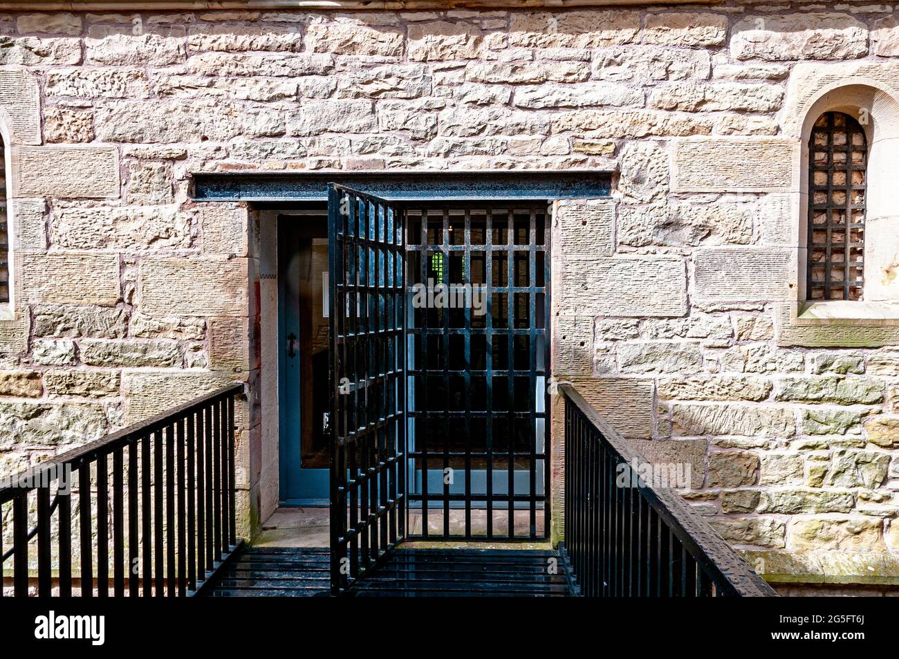 Eine Glasschiebetür, die durch ein Stahlgitter geschützt ist, verbindet das Gefängnishaus über einen gusseisernen Gang mit dem Bridewell-Zellblock im alten Gefängnis von Jedburgh Stockfoto