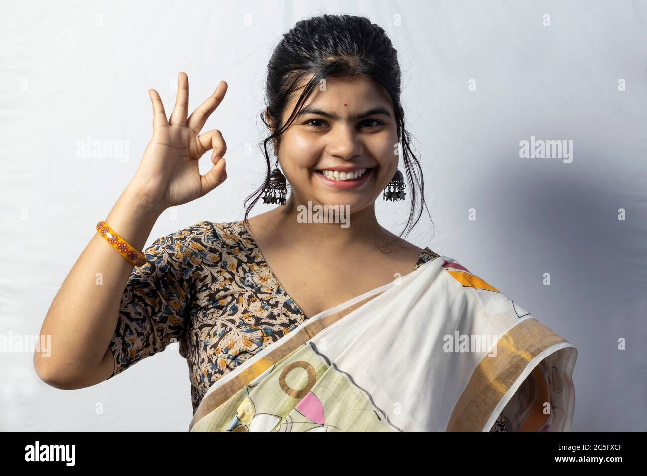 Isoliert auf weißem Hintergrund zeigt ein indisches Weibchen in Saree eine gute Geste mit lächelndem Gesicht auf weißem Hintergrund Stockfoto