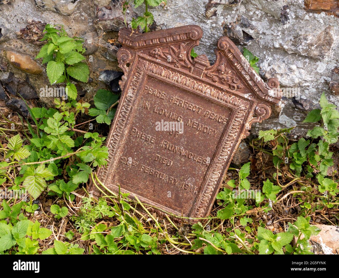 Eine dekorative Wandtafel aus Gusseisen als Grabmarker, die an einer Steinwand und Unterholz in Bruisyard Church Grabstein, Suffolk, Großbritannien, liegt Stockfoto