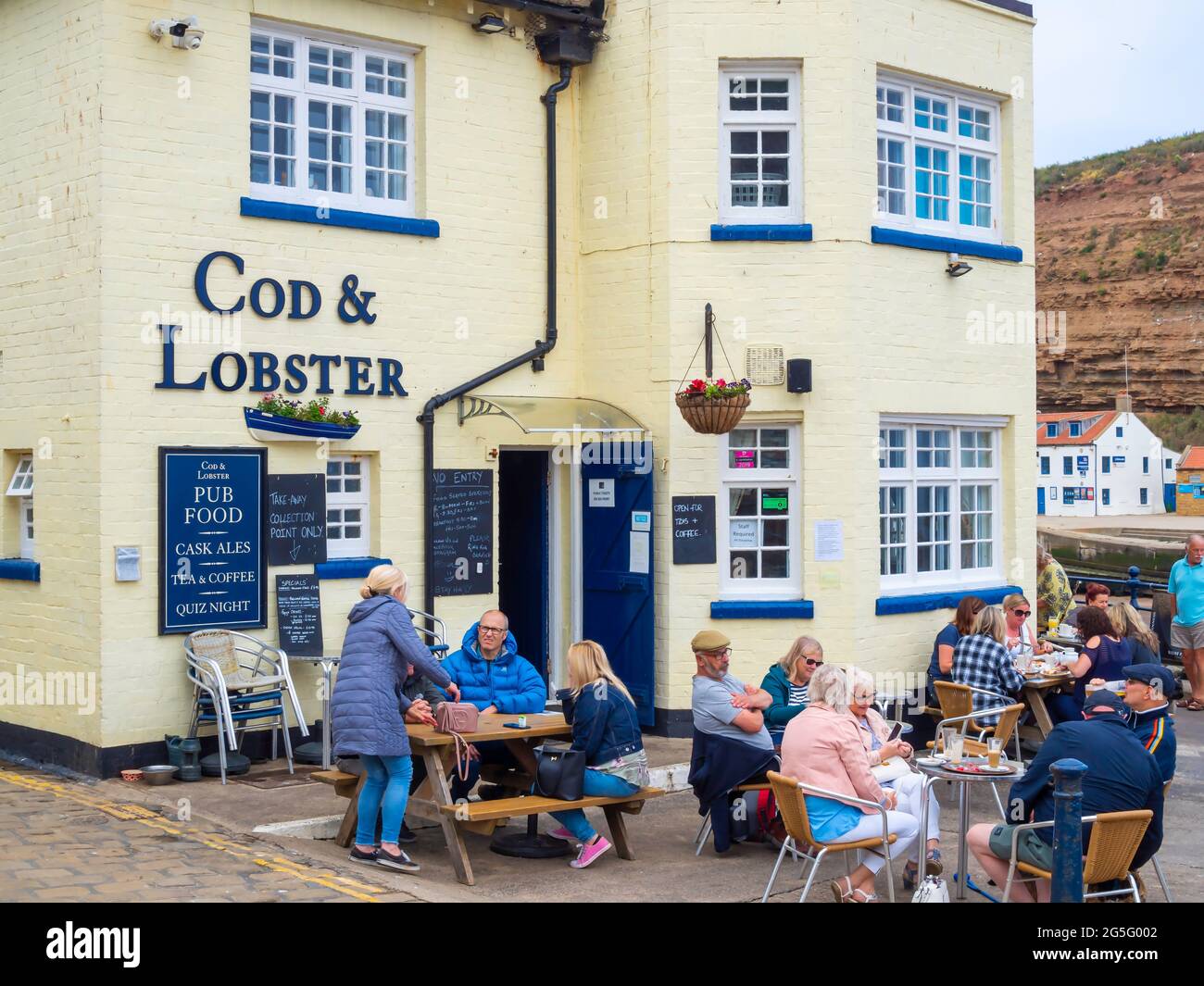 Eine Menge Leute, die im Sommer vor dem Cod and Lobster Pub am Hafen von Staithes North Yorkshire essen Stockfoto