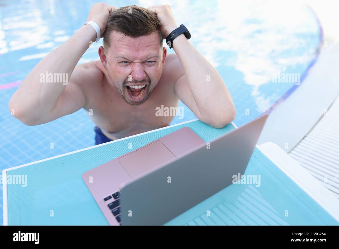 Mann schwimmt im Pool und reißt sich die Haare vor dem Laptop-Bildschirm Stockfoto