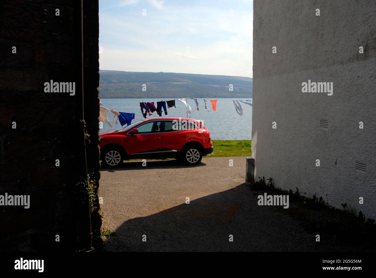 Inländische Szene in Inveraray, Argyll & Bute, Schottland, mit einem hinter dem Gebäude geparkten Auto und einer Waschmaschine, die an der Linie neben Loch Fyne hängt Stockfoto