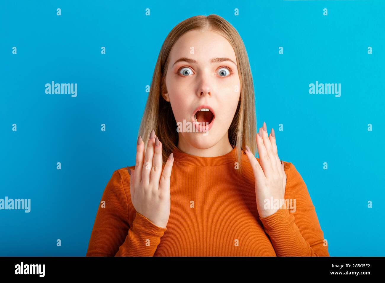 Emotionales Porträt einer überraschten Frau mit offenem Mund und offenen Händen. Nahaufnahme-Porträt eines Teenagers auf isoliertem blauem Hintergrund. Stockfoto