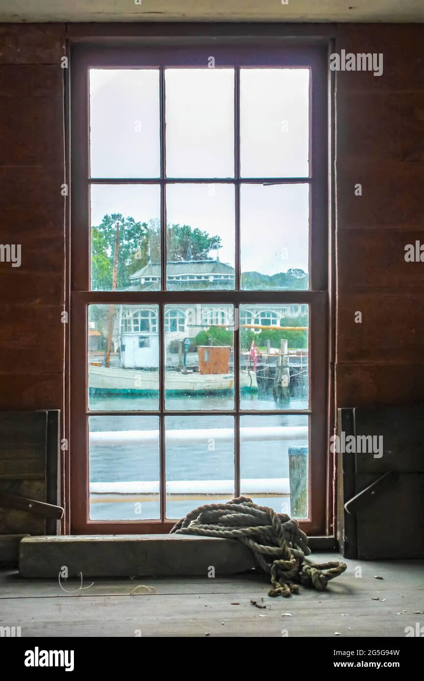 Blick aus schmutzigen grungy Paned Fenster an regnerischen Tag von Werkstatt Gebäude mit Seil auf einem Regal zu anderen Marina Gebäude und Wasser und festgemacht Boot Stockfoto