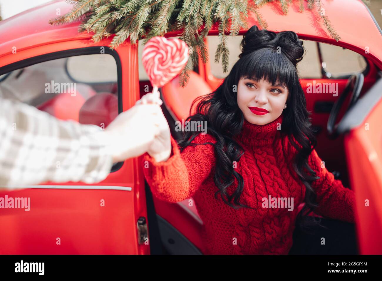 Schöne dunkelhaarige Dame in rotem Pullover, die aus dem Auto aussteigen Stockfoto