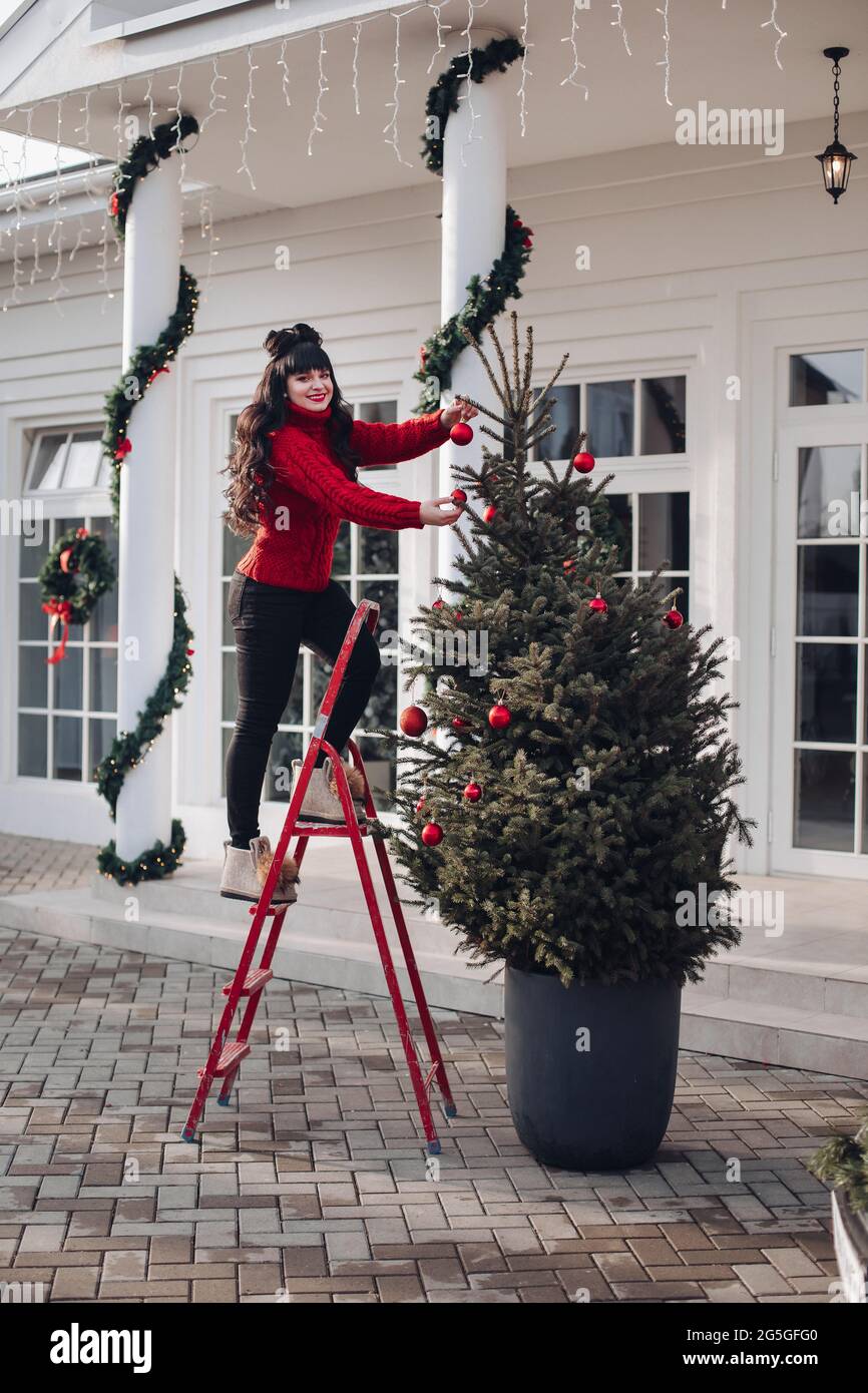 Fröhliche Frau, die Leiter benutzt, um Ornamente auf Weihnachtsbaum zu  setzen Stockfotografie - Alamy
