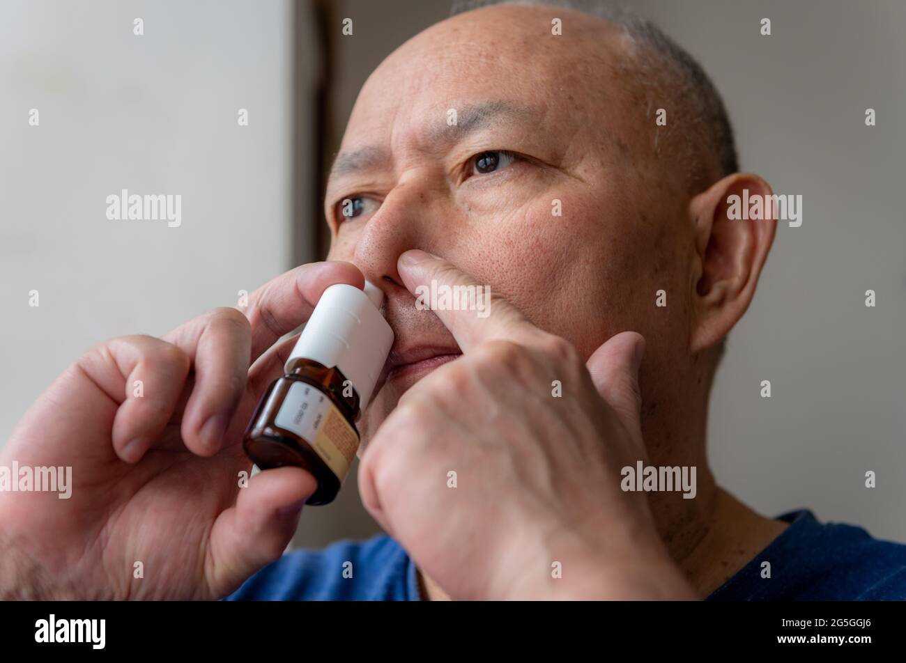 Ein reifer Mann, der an Heuschnupfen leidet und zur Linderung der Symptome ein Nasenspray einsprüht. Stockfoto