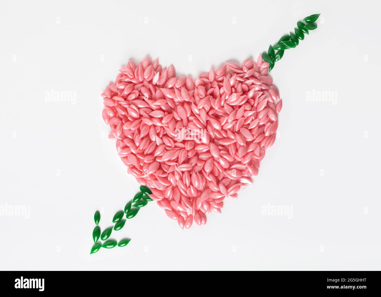 Enthaarungswachs-Granulat wird in Form eines Herzens auf weißem Hintergrund mit einem Pfeil ausgelegt. Konzept der Liebe zur Haarentfernung und Hautglättung. Stockfoto