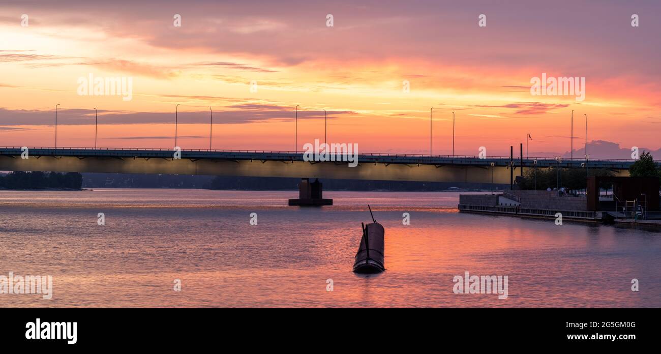 Helsinki / Finnland - 26. JUNI 2021: Eine schwimmende Wellenbrecher vor einer beleuchteten Brücke gegen den leuchtend roten Himmel bei Sonnenuntergang. Stockfoto