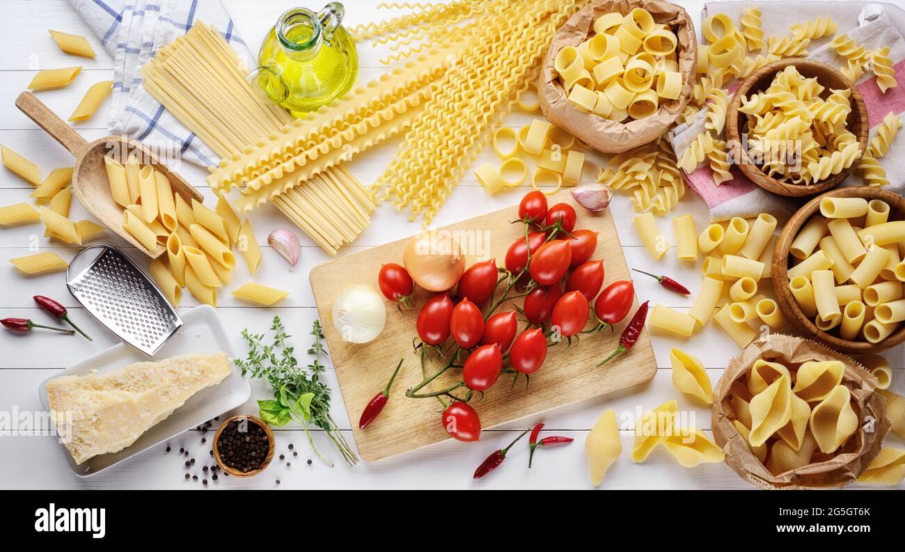 Pasta und Zutaten: Tomaten, Parmigiano, natives Olivenöl extra, Penne, Muscheln, Rigatoni, mafalda, Linguine, Fusilli und Tintenfisch auf weißem Holzbac Stockfoto