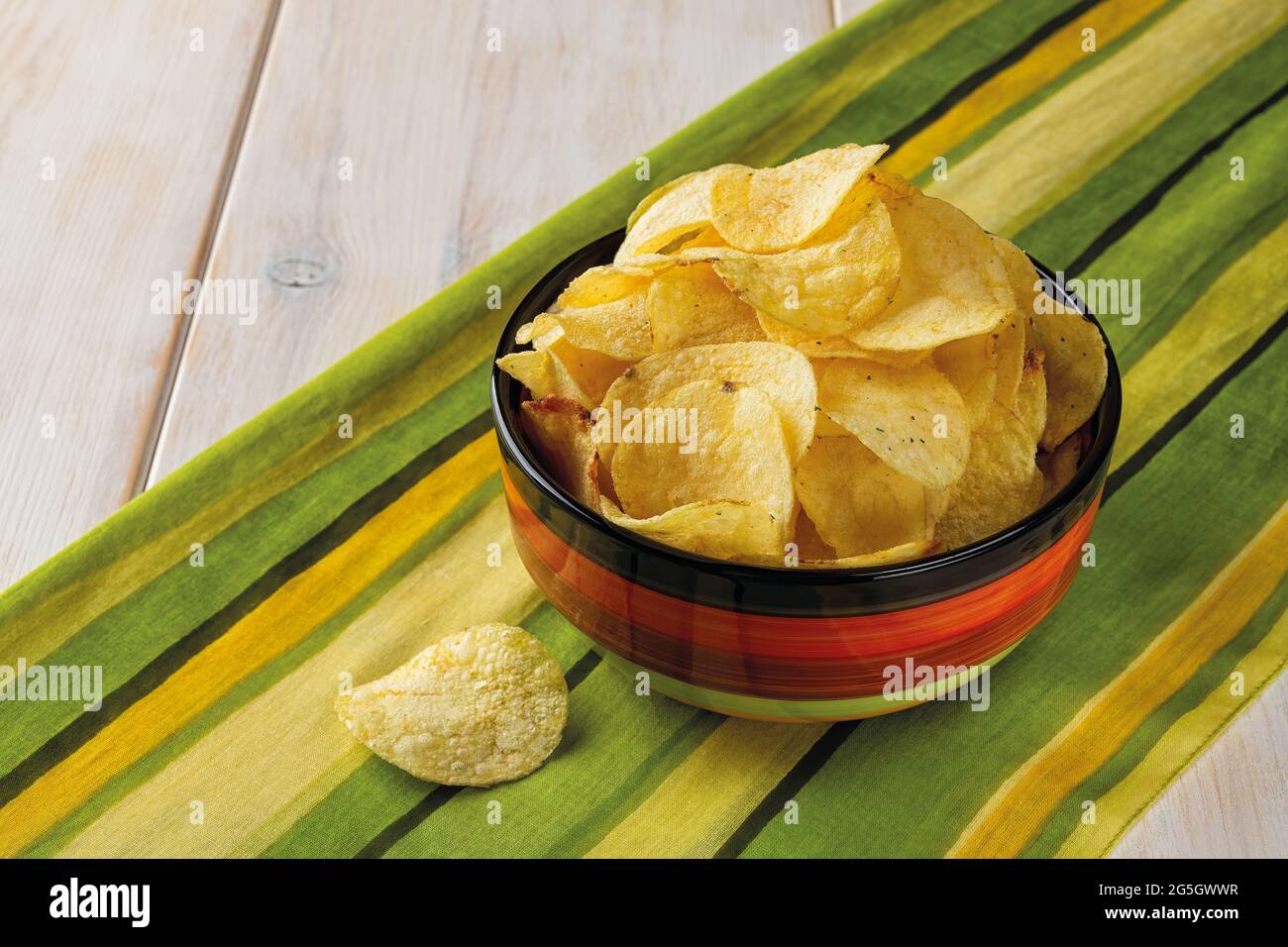 Knusprige Kartoffelchips mit Dill in einer Keramikschale über gestreifte gelbgrüne Tischserviette. Beliebte Snack von Kartoffeln frittierten dünnen Scheiben. Fast Food. Stockfoto