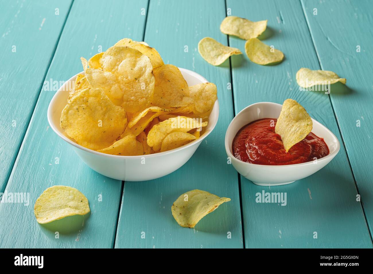 Leckere Kartoffelchips mit Dill und dickem Tomatenketchup in weißen Keramikschalen über dem Holztisch. Knuspriger Snack aus Kartoffeln frittierte dünne Scheiben. Stockfoto