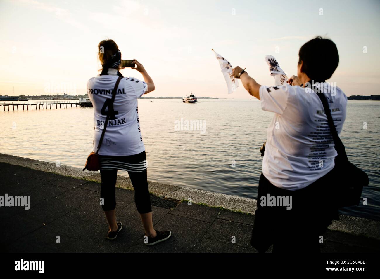 Kiel, Deutschland. Juni 2021. Fans des deutschen Handballmeisters THW Kiel jubeln dem Team zu. Mit der Elektrofähre 'MS Düsternbrook' waren die Kieler Handballer entlang der Wasserstraße in die Kiellinie gefahren, um sich und den WM-Pokal den wartenden Anhängern zu präsentieren. Die Kielers hatten am 27.06.2021 ihren 22. DM-Titel gewonnen. Quelle: Frank Molter/dpa/Alamy Live News Stockfoto