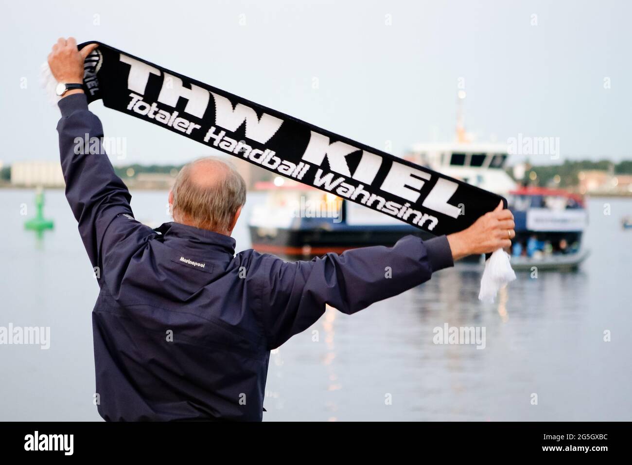 Kiel, Deutschland. Juni 2021. Ein Mann hält einen Schal des deutschen Handballmeisters THW Kiel in den Händen und jubelt vom Ufer aus für das Team. Mit der Elektrofähre 'MS Düsternbrook' waren die Kieler Handballspieler auf dem Wasser entlang der Kiellinie gereist, um sich und den WM-Schal den wartenden Anhängern zu präsentieren. Die Kielers hatten am 27.06.2021 ihren 22. DM-Titel gewonnen. Quelle: Frank Molter/dpa/Alamy Live News Stockfoto