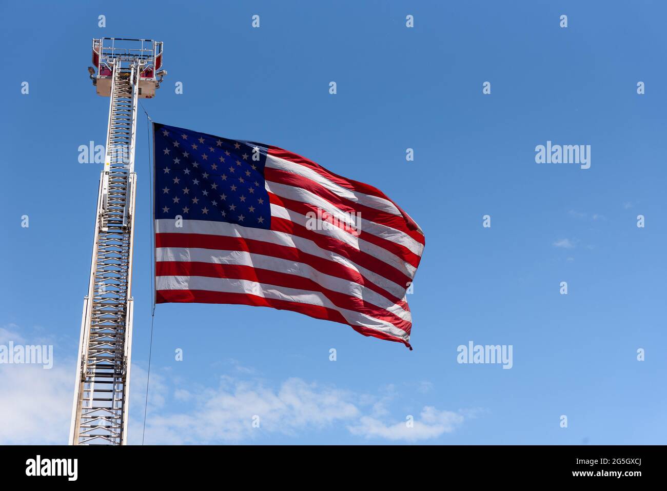 Eine große US-Flagge, ein Symbol für Freiheit und Freiheit, fliegt im Wind, befestigt an einer hoch aufragenden Feuerwehrleiter. Stockfoto