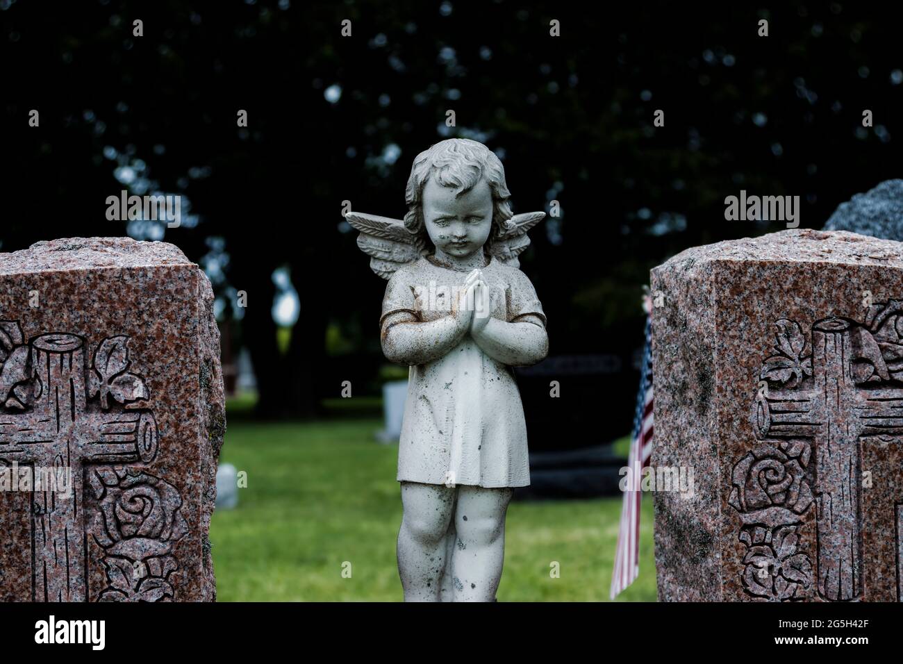 Alte Engelsstatue auf einem Friedhof - kindliche Figur mit gebetteten Händen Stockfoto