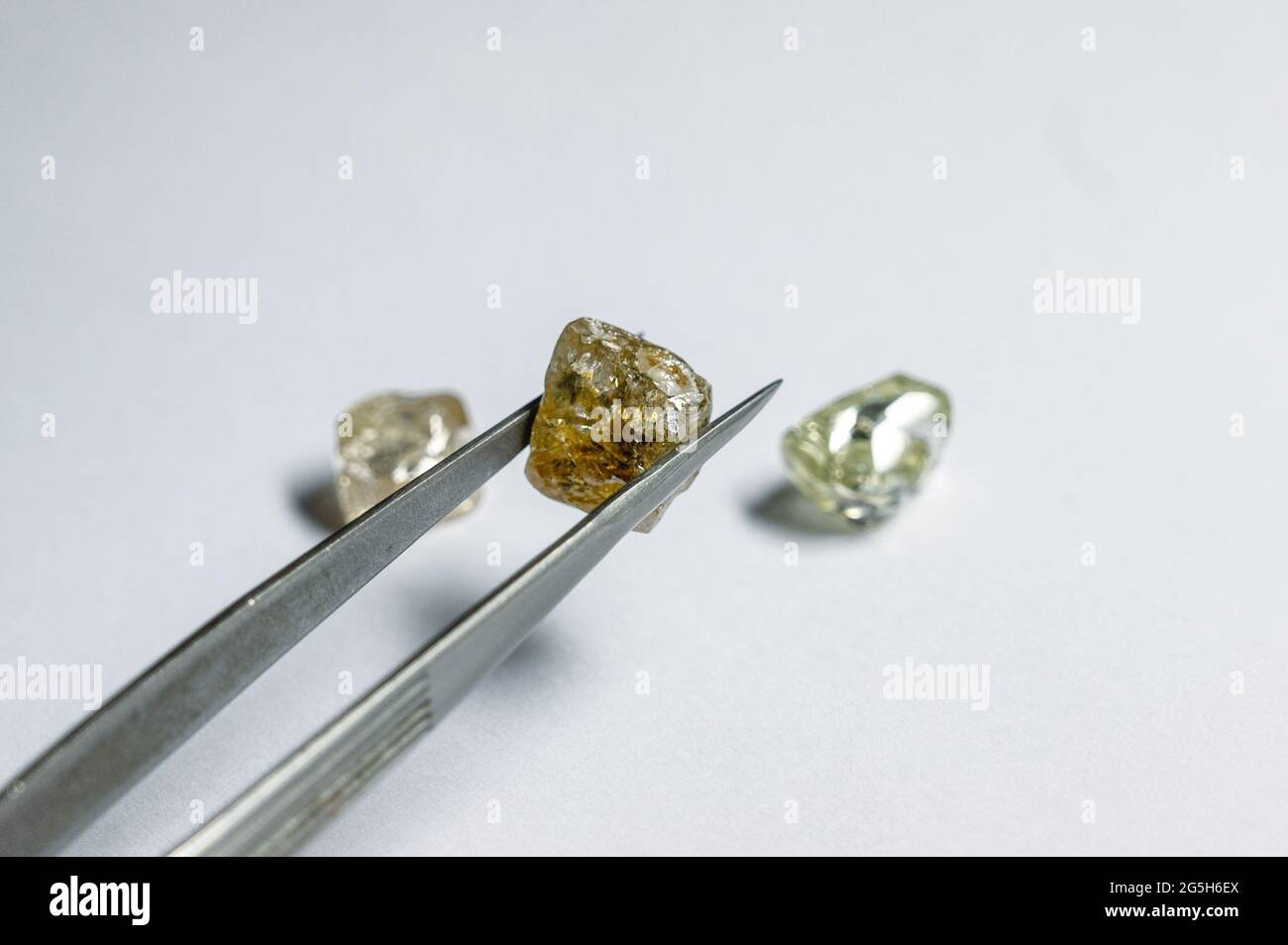 Der farbige Diamant wird mit einer Metallpinzette gehalten. Zwei weitere Edelsteine liegen in der Nähe Stockfoto
