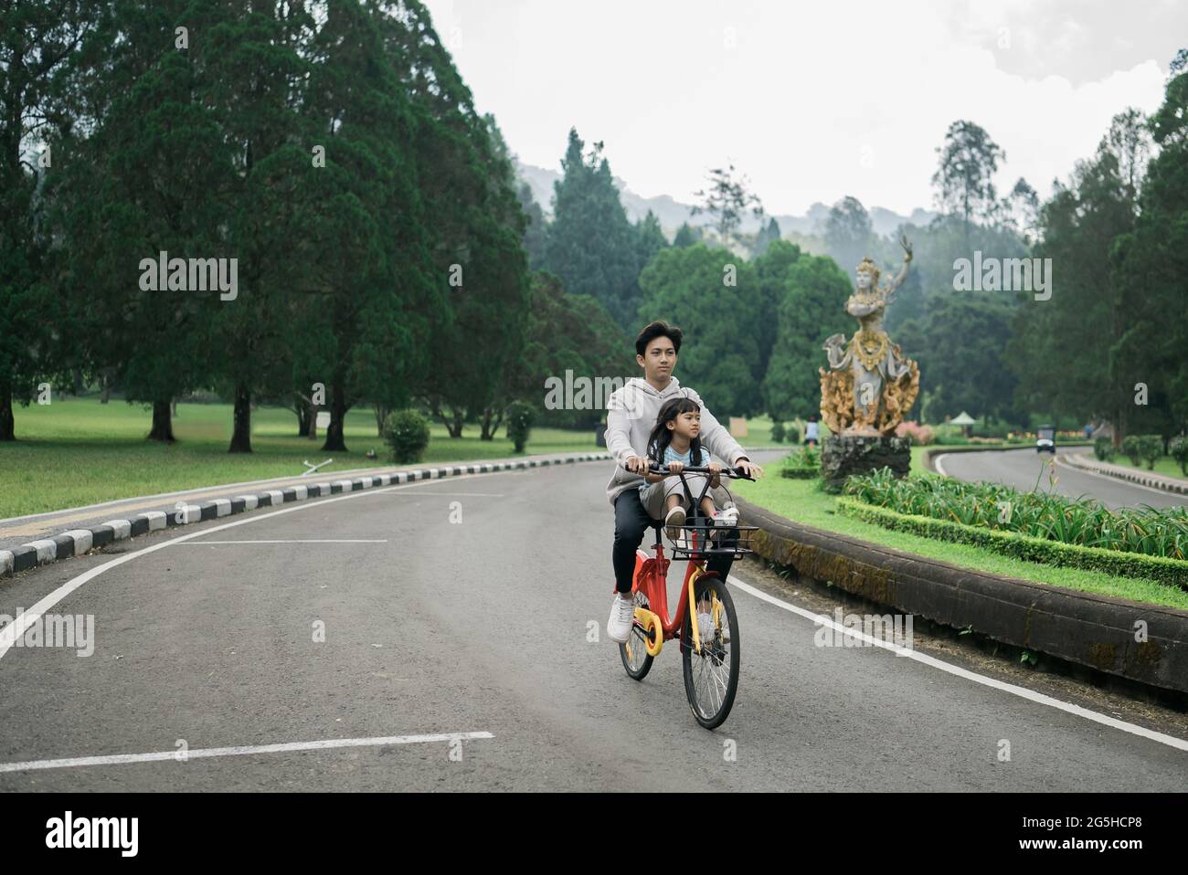 Bruder nimmt seine Schwester mit auf lustige Fahrradtour im Park Stockfoto