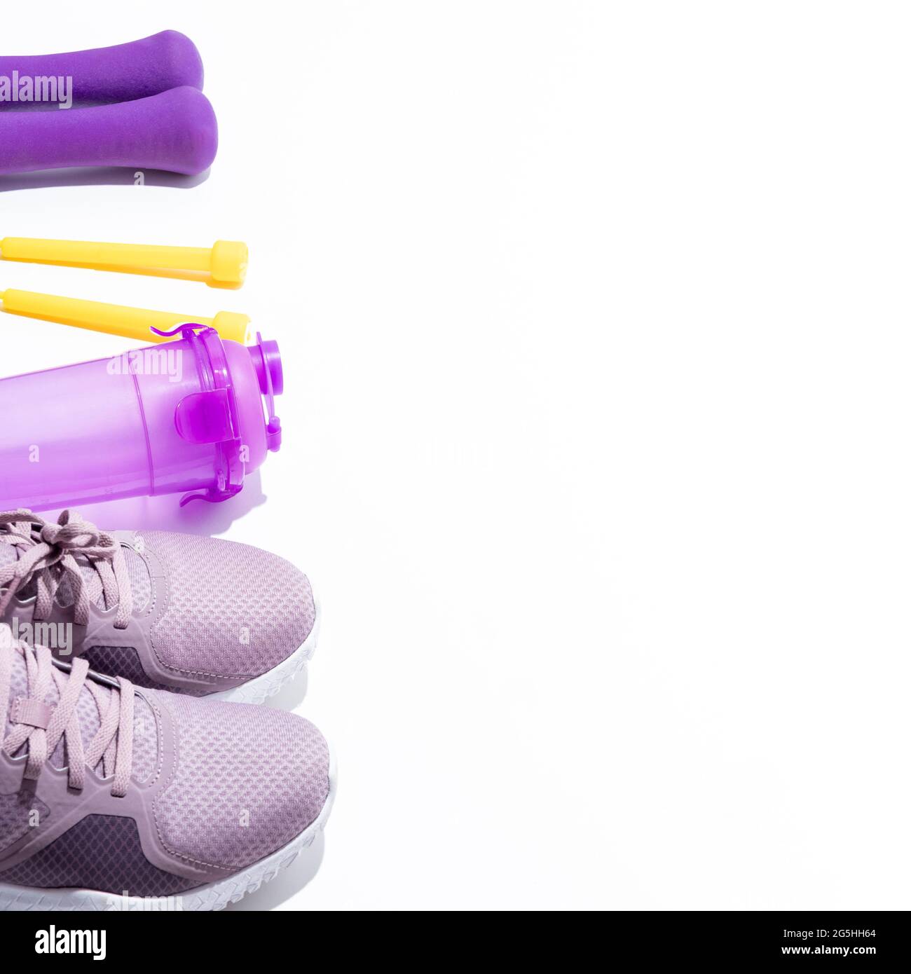 Lila Sneaker, Hanteln, Wasserflasche, gelbes Springseil auf weißem Hintergrund mit Platz für Text. Selektiver Fokus. Stockfoto