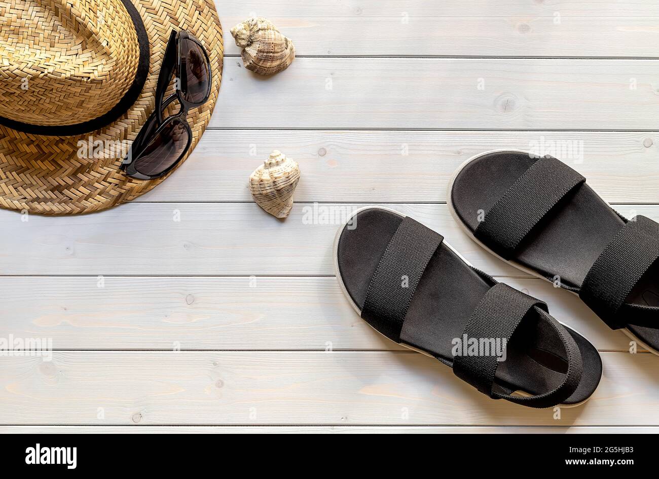 Schwarze Sandalen mit offenem Zehenbereich aus recycelten Kunststofffasern, Strohhut, Sonnenbrille und Muscheln für Damen Stockfoto