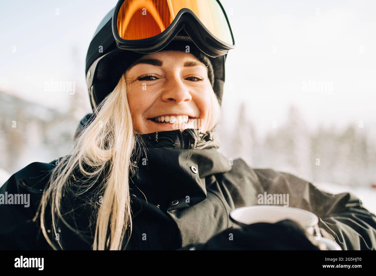 Porträt einer lächelnden blonden Frau mit Skibrille und Helm Stockfoto