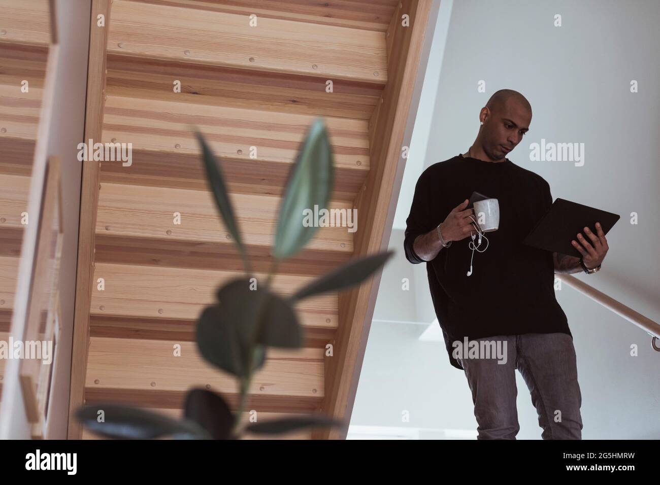 Männlicher Unternehmer, der ein digitales Tablet verwendet, während er den Kaffeebecher zu Hause hält Stockfoto