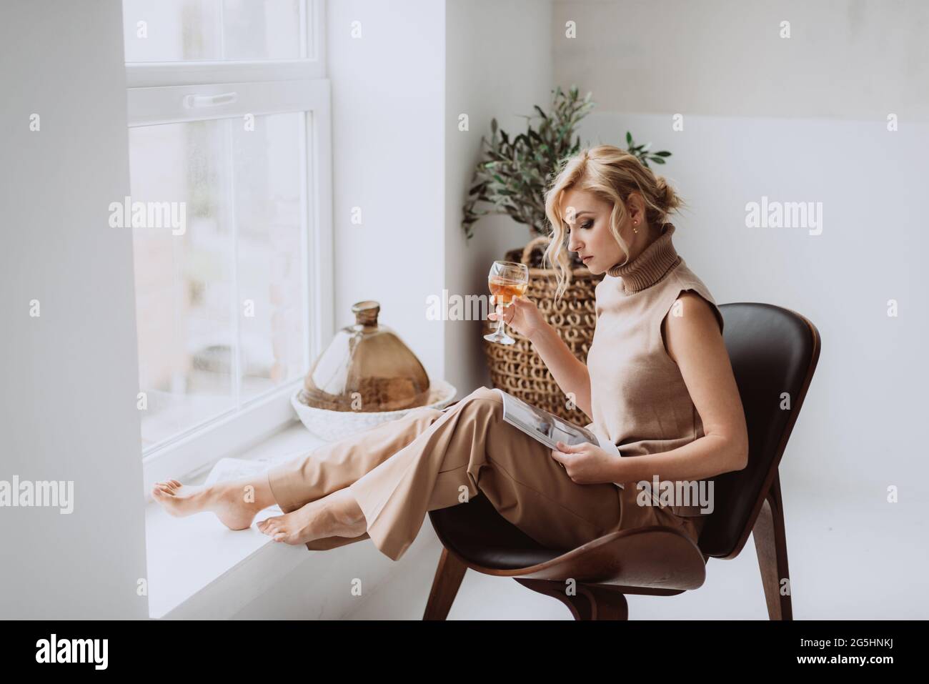 Junge Geschäftsfrau arbeitet zu Hause. Das nachdenkliche, ruhige Model hält ein Glas Weißwein und liest ein Magazin. Schöne Frau in einem modernen Interieur. Weiches Sel Stockfoto