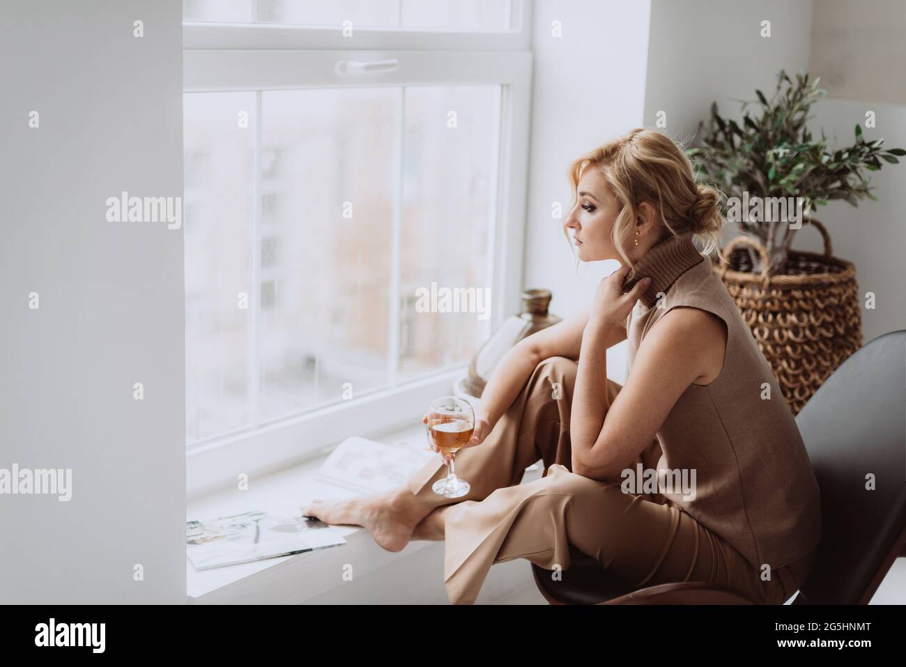 Junge Geschäftsfrau arbeitet zu Hause. Das nachdenkliche, ruhige Modell hält ein Glas Weißwein und blickt aus dem Fenster. Schöne Frau in einem modernen Interieur. Weich Stockfoto