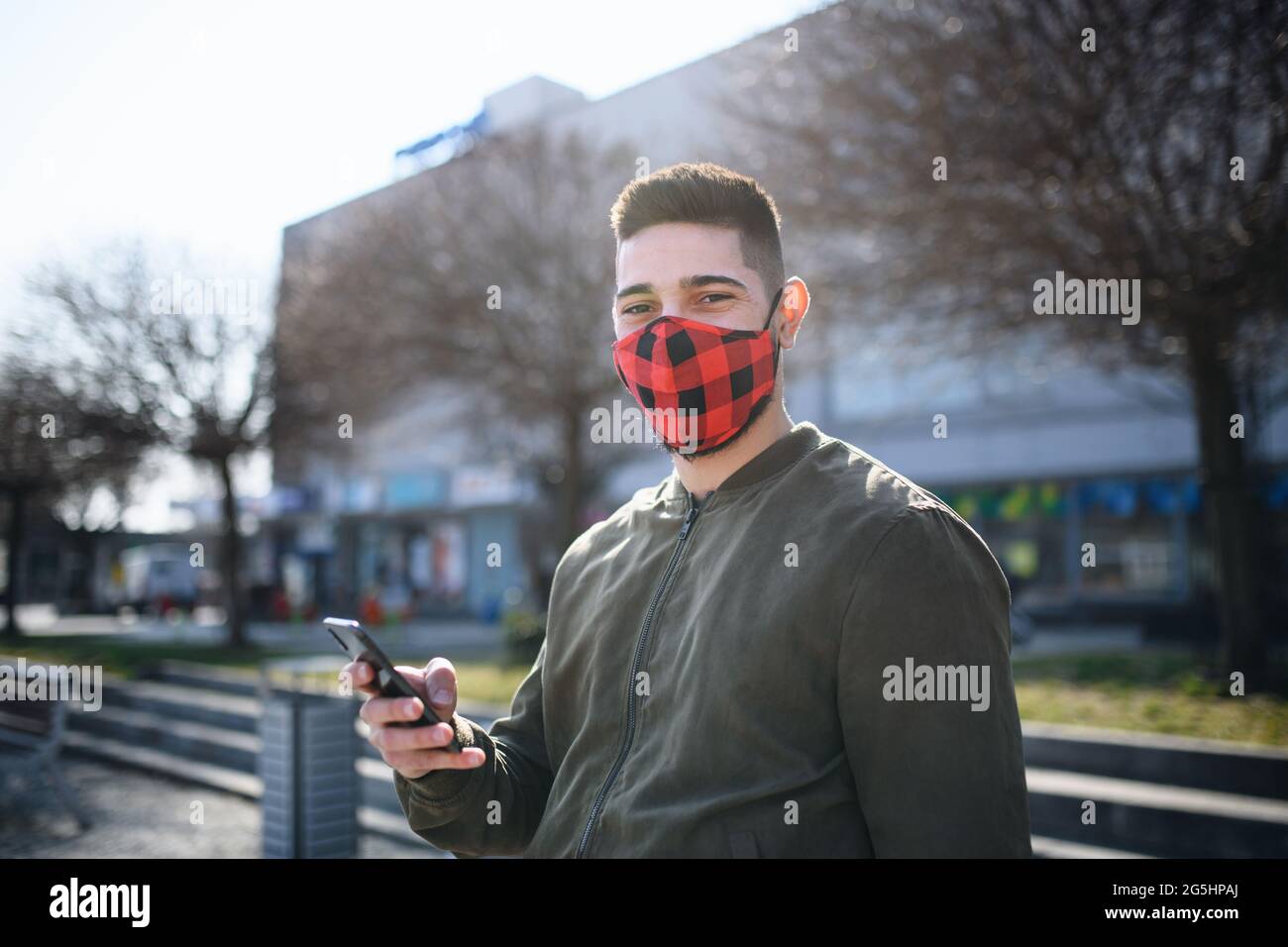 Junger Mann im Freien auf der Straße in der Stadt mit Smartphone, Coronavirus und neuem normalen Konzept. Stockfoto
