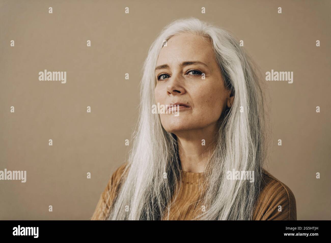 Selbstbewusste reife Frau mit weißem Haar vor beigem Hintergrund Stockfoto