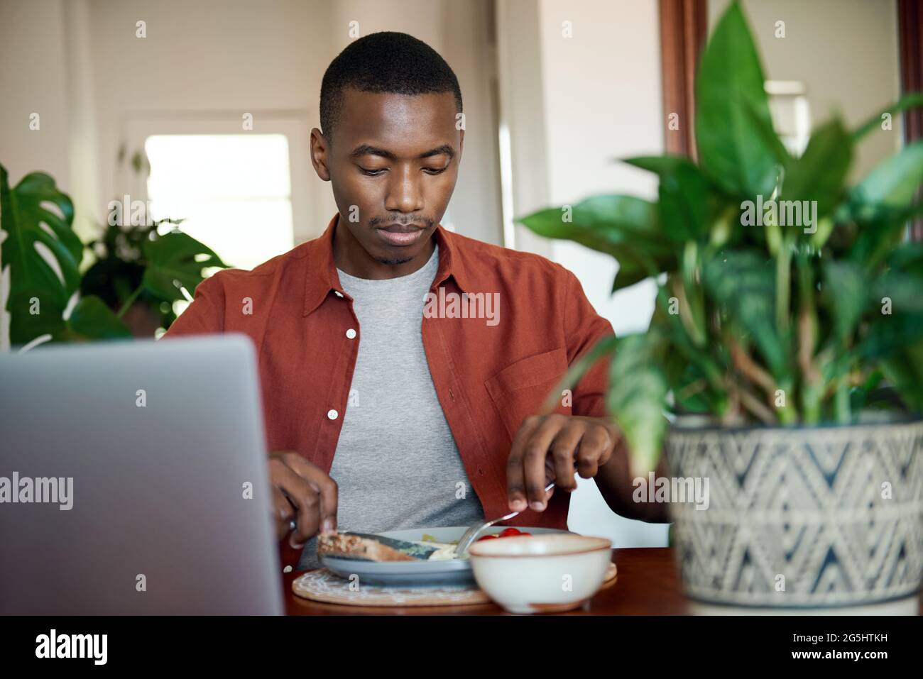 Junger afrikanischer Mann, der beim Frühstück einen Laptop benutzt Stockfoto