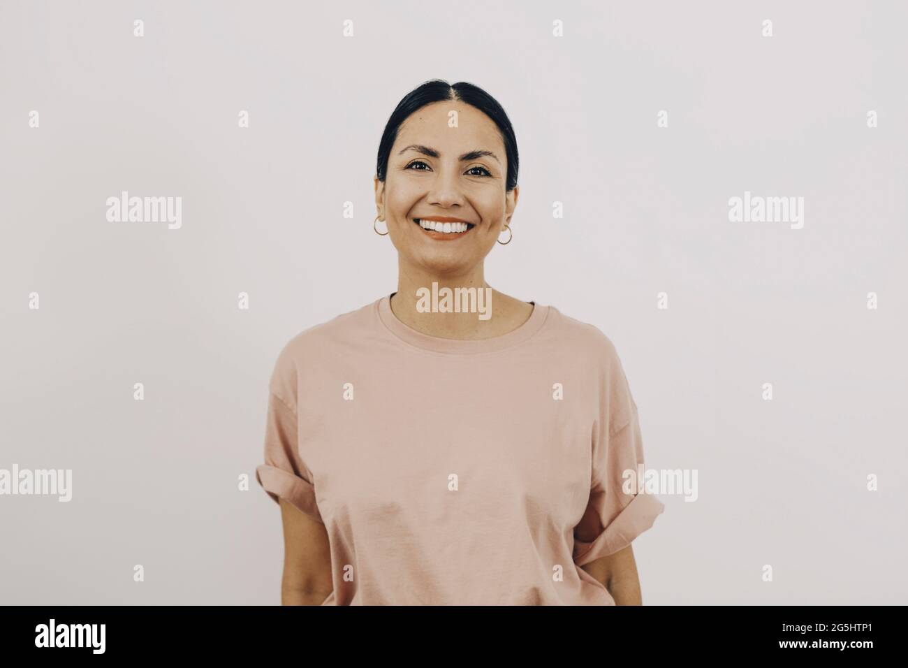 Porträt einer lächelnden Frau in pfirsichfarbenem T-Shirt auf weißem Hintergrund Stockfoto
