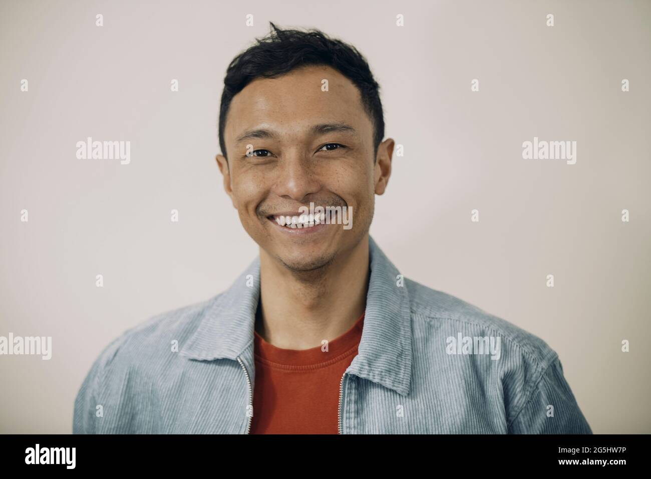Porträt eines lächelnden Mannes mit blauer Jacke auf beigefarbenem Hintergrund Stockfoto