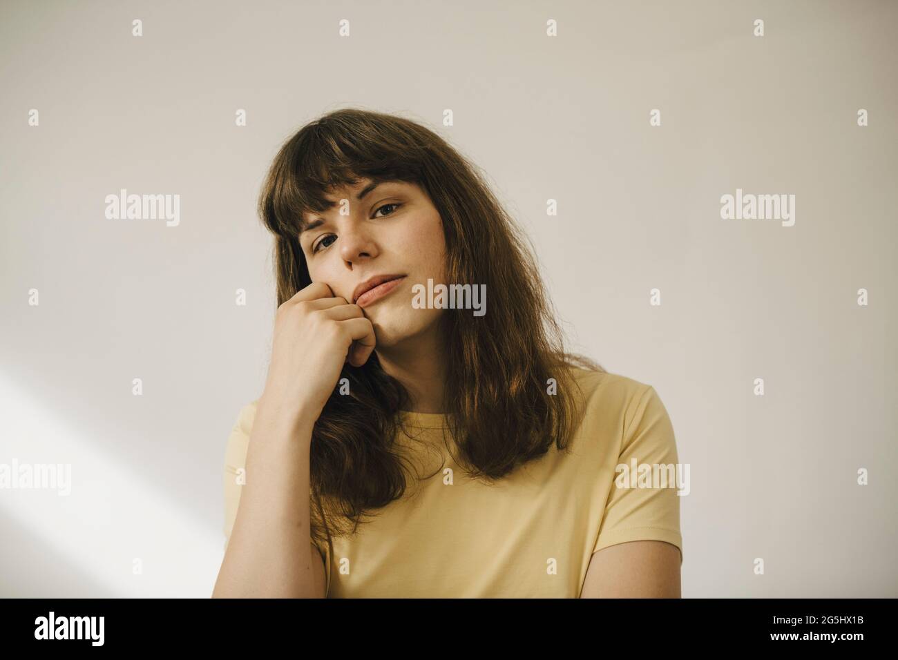 Junge Frau mit der Hand am Kinn vor der weißen Wand Stockfoto
