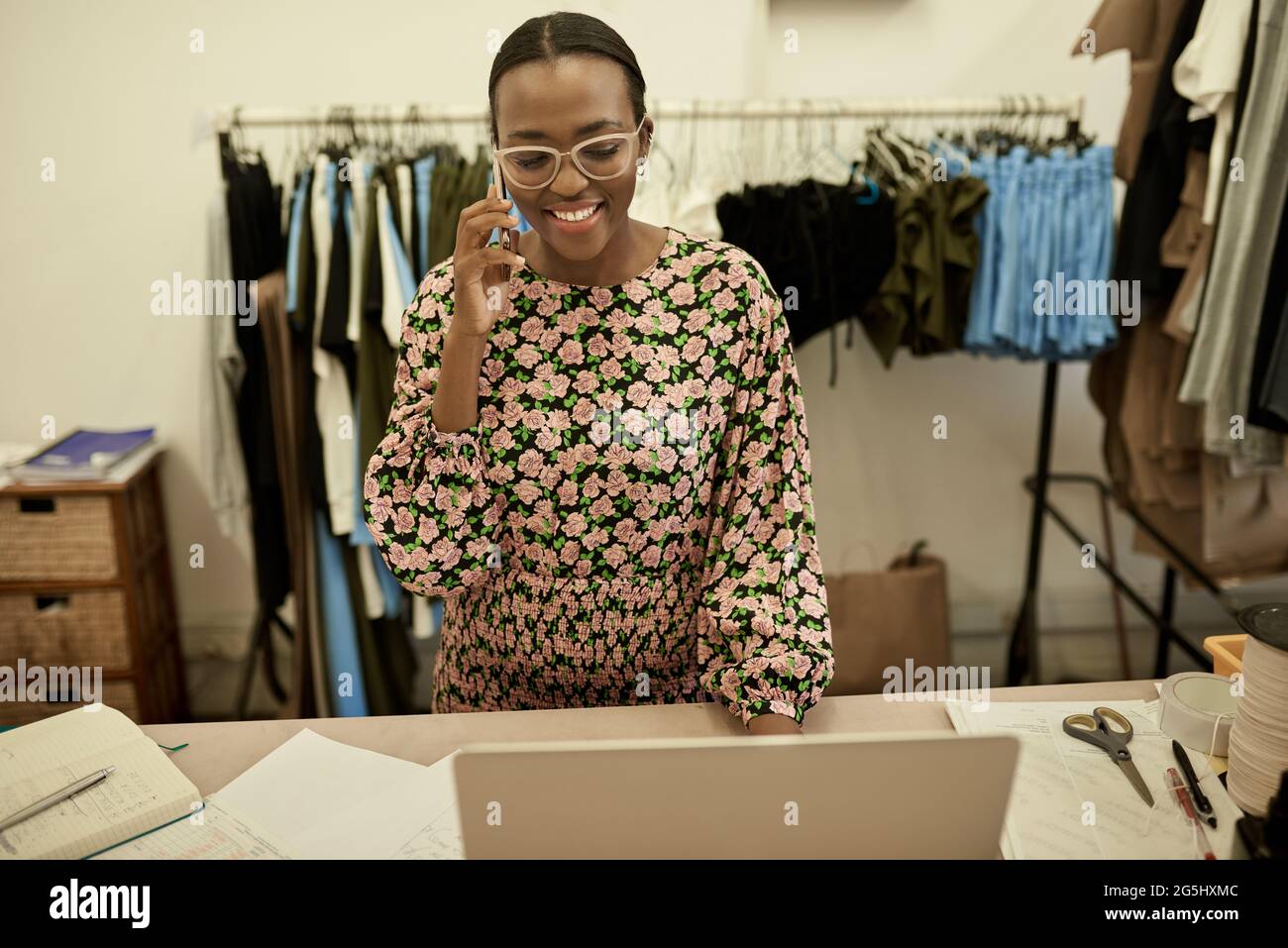 Lächelnde afrikanische Modedesignerin spricht in ihrem Studio am Telefon Stockfoto