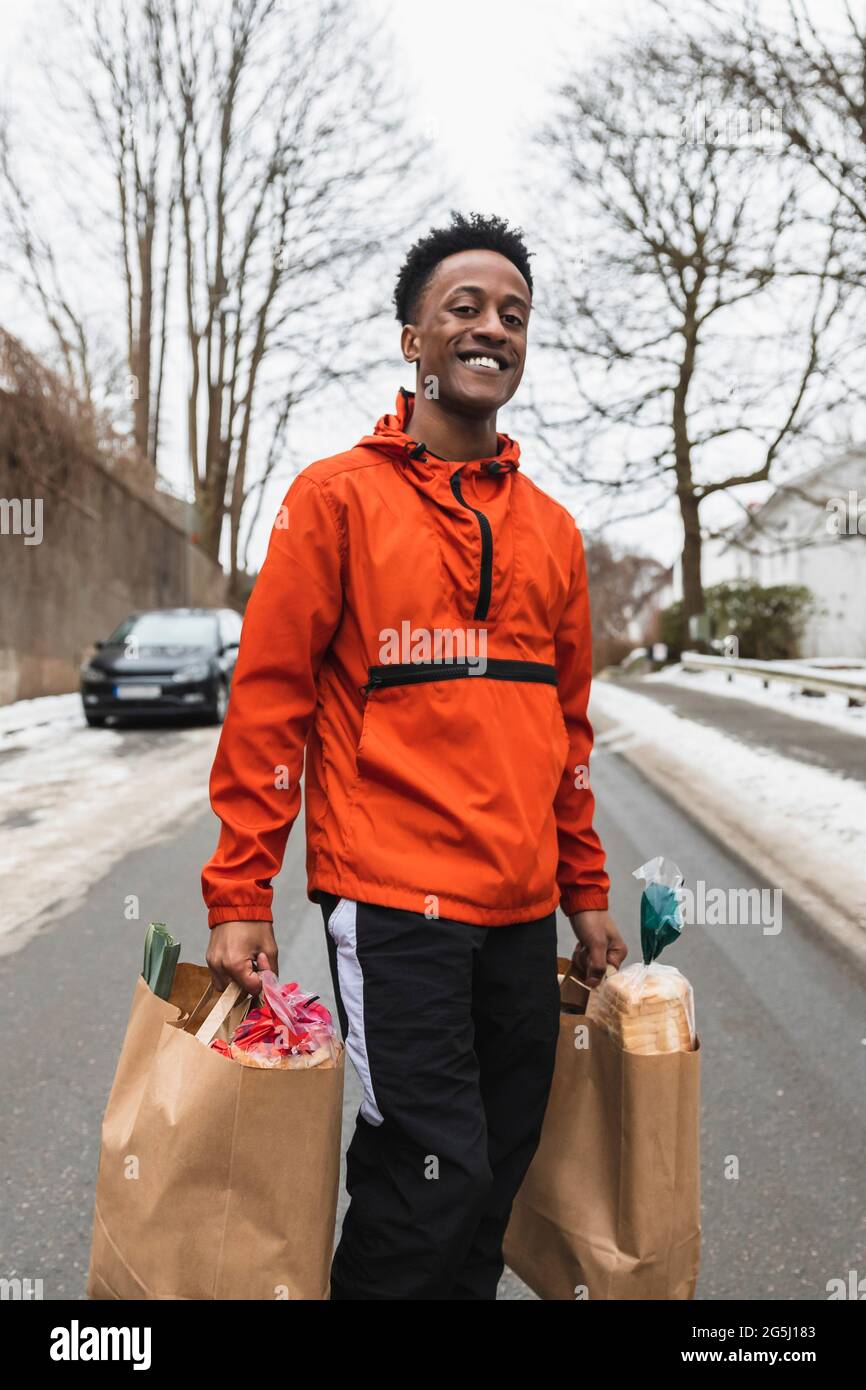 Porträt eines lächelnden Mannes, der Papiertüten trägt, während er auf der Straße unterwegs ist Stockfoto
