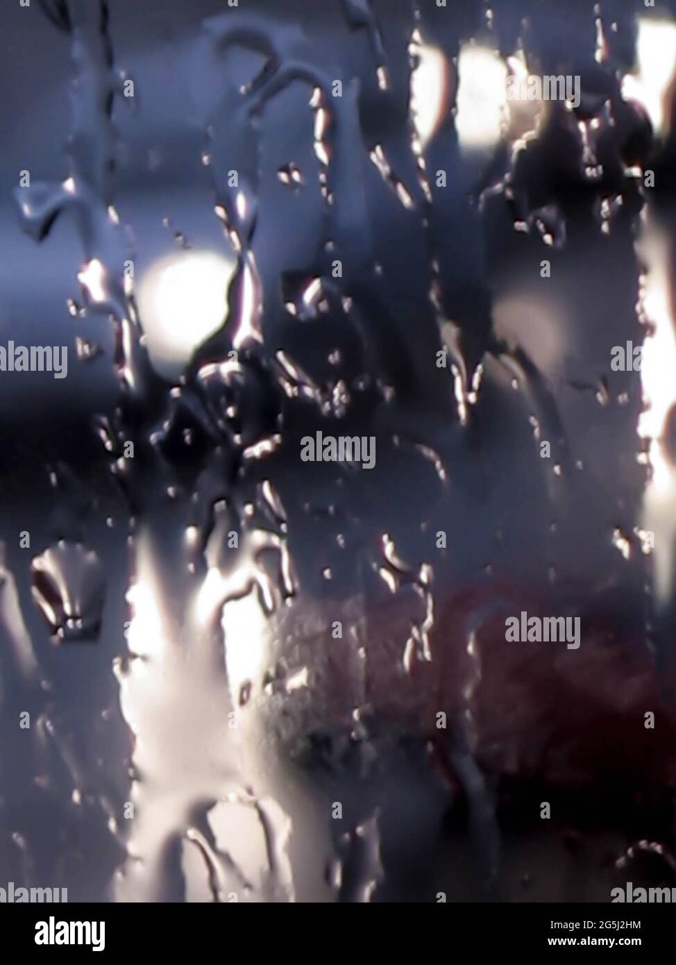 Verschwommener abstrakter, launischer Nahaufnahme-Hintergrund von Regentropfen bei schlechtem Wetter, die gegen ein nasses, transparentes Glasfenster spritzen. Stockfoto