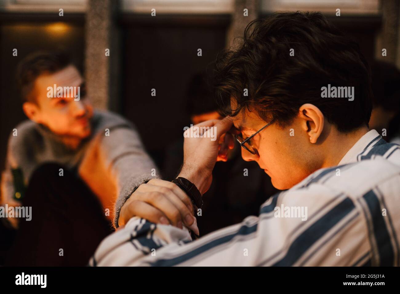 Junger Mann, der die Hand eines besorgten männlichen Freundes auf dem Balkon hält Stockfoto