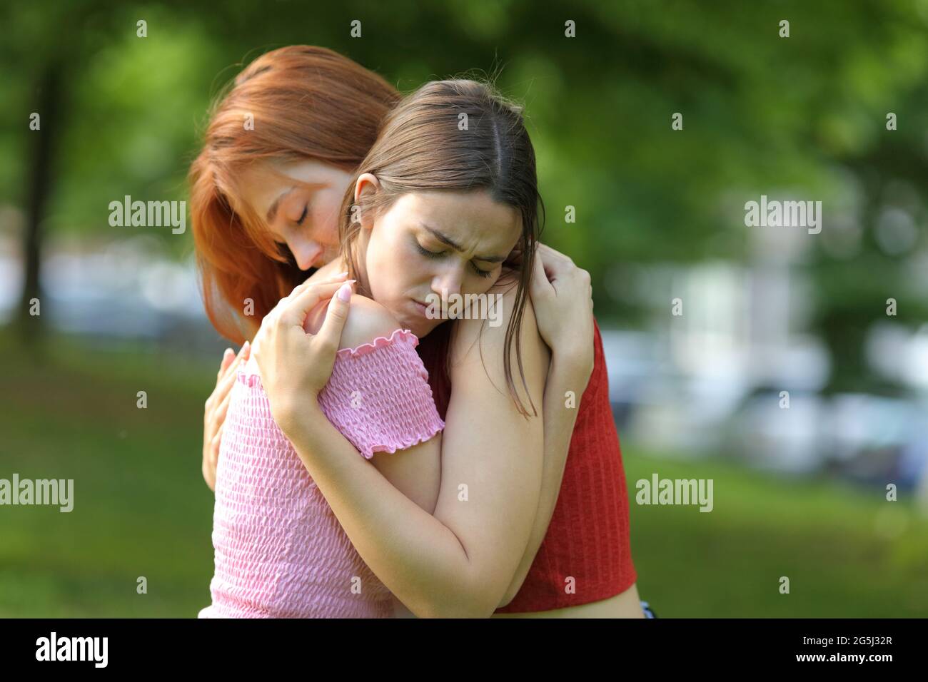 Traurige Mädchen, die sich versöhnten, nachdem sie sich in einem Park umarmten Stockfoto