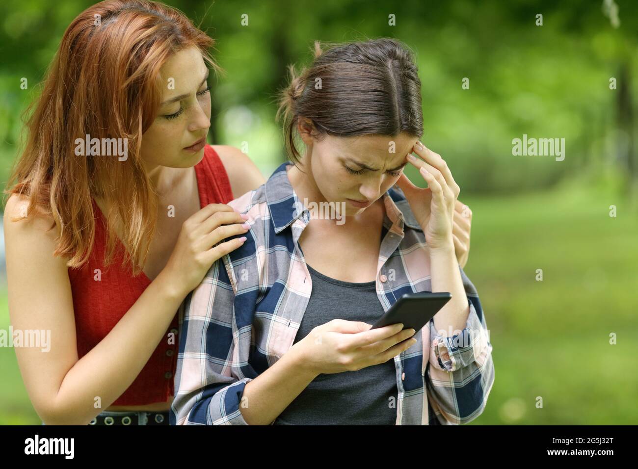Ein trauriger Student, der auf dem Smartphone nachgeht und von einem Freund in einem Park oder auf dem Campus getröstet wird Stockfoto