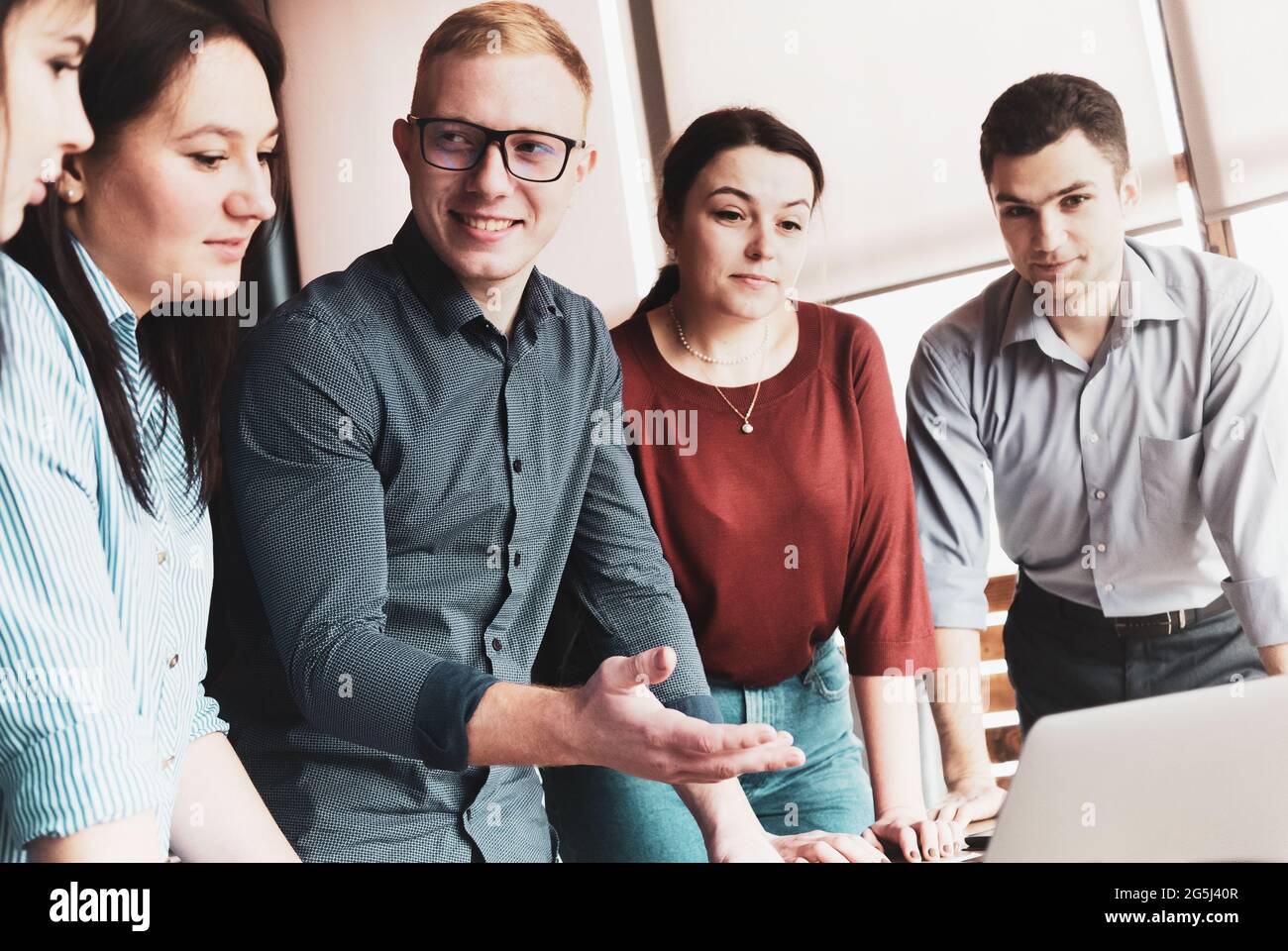 Junger Geschäftsmann, der in einem gemeinsamen Treffen seine Kollegen anschaut und eine Handbewegung zum Computer macht - Konzept der Zusammenarbeit und Teamarbeit - Stockfoto