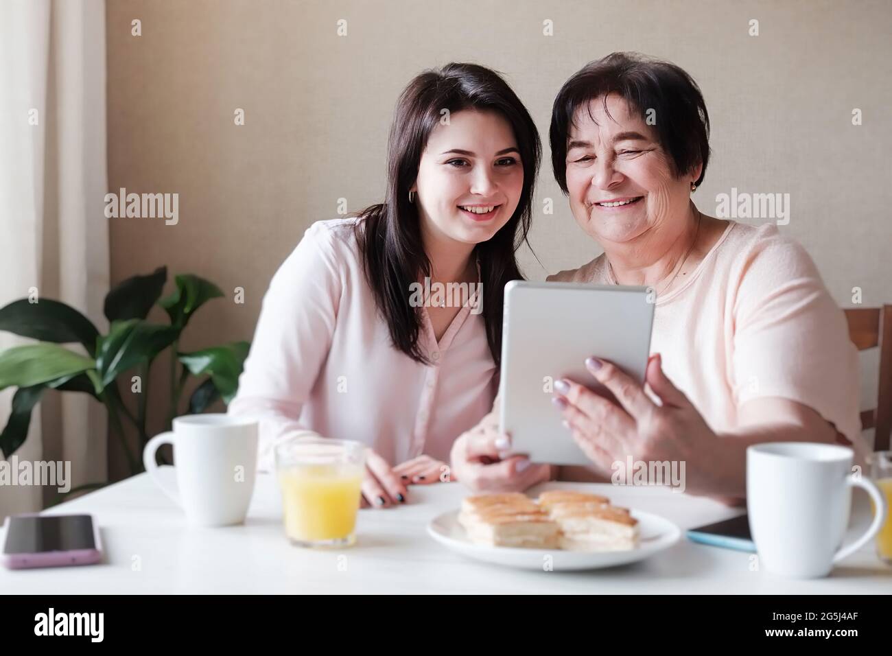 Eine ältere Mutter und eine Erwachsene Tochter haben Spaß zu Hause mit einem Tablet, um Inhalte im Internet zu sehen - echte Familienbeziehungen von verschiedenen Stockfoto