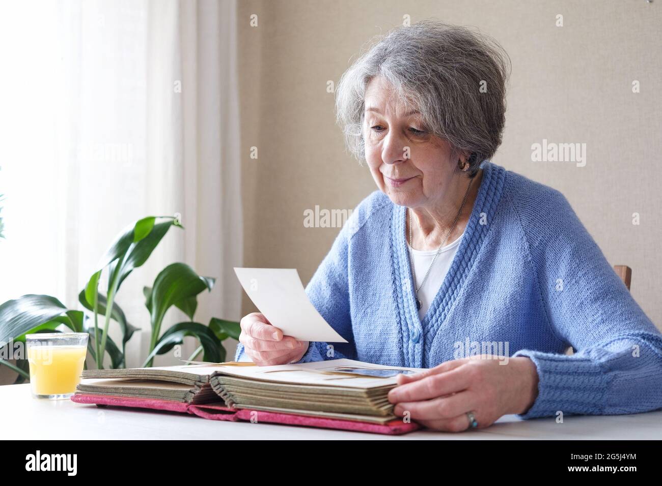 Eine ältere Frau mit Nostalgie betrachtet alte Fotos in einem Fotoalbum oder Fotobuch - das Konzept von Familie und Lebenswerten und Einsamkeit im Alter Stockfoto