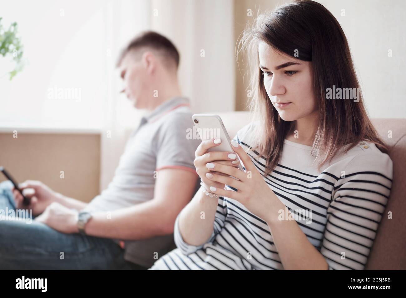 Verärgerte Ehemann und Ehefrau oder Freund und Freundin sitzen auf der Couch und schauen sich das Telefon an - verärgerte junge Menschen ignorieren sich gegenseitig und Stockfoto
