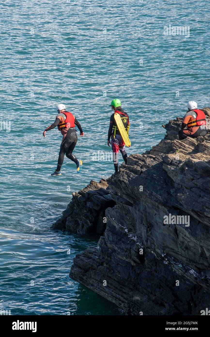 Ein Urlauber, der an der Küste von Towan Head in Newquay in Cornwall von Felsen ins Meer springt. Stockfoto