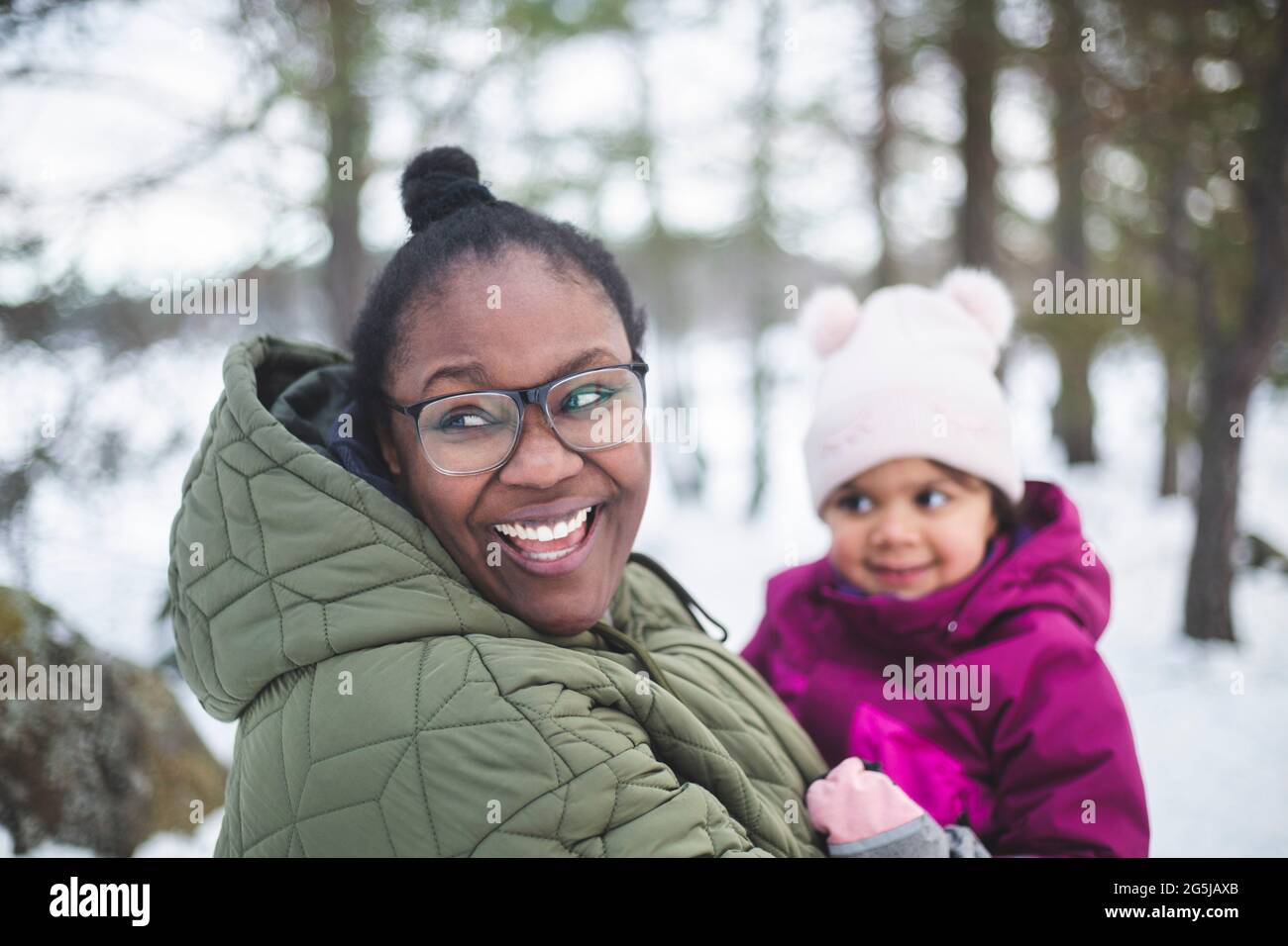 Fröhliche Frau, die Tochter trägt, während sie wegschaut Stockfoto