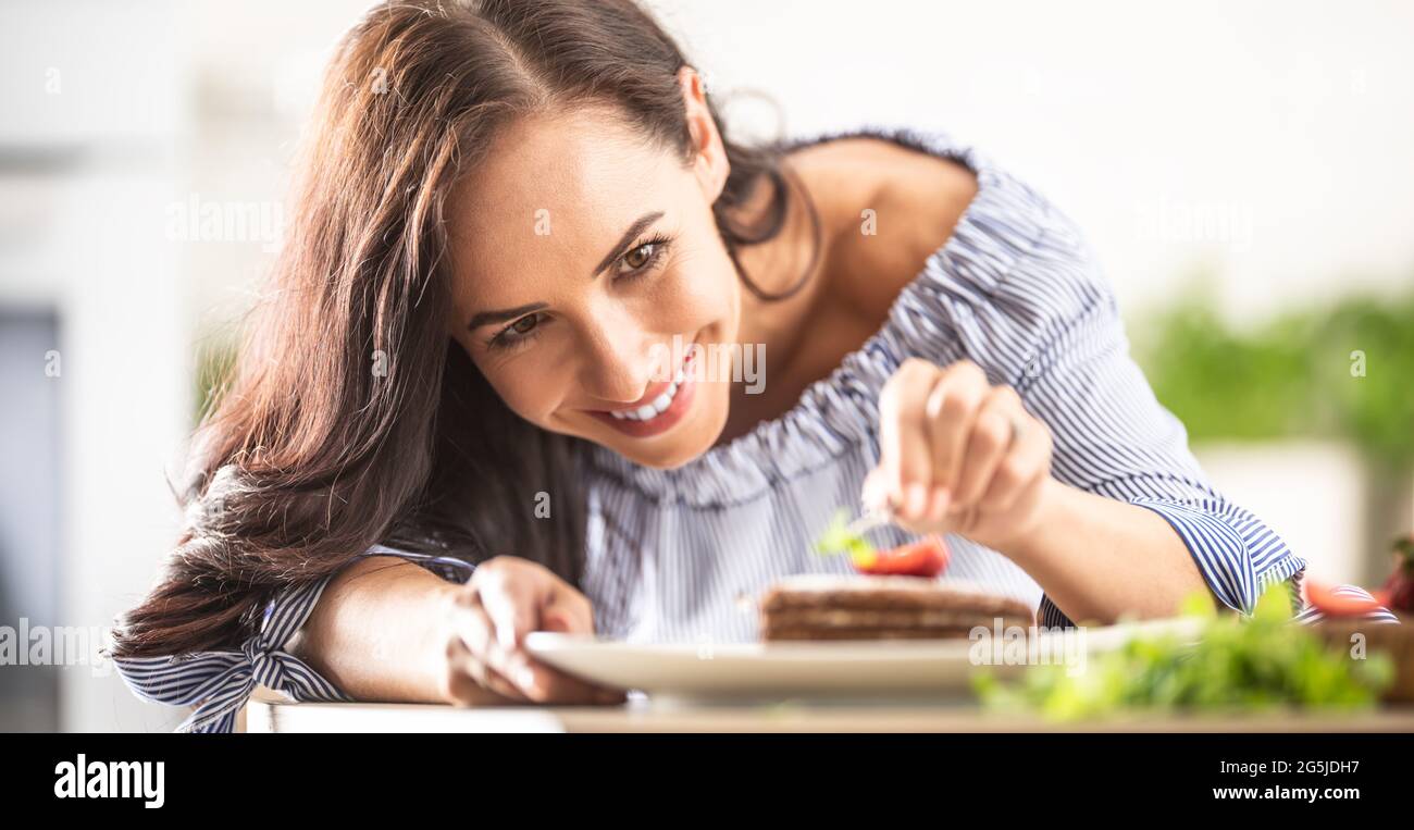 Frau macht den letzten Schliff einer Kuchendekoration, indem sie Minzblatt darauf legt. Stockfoto