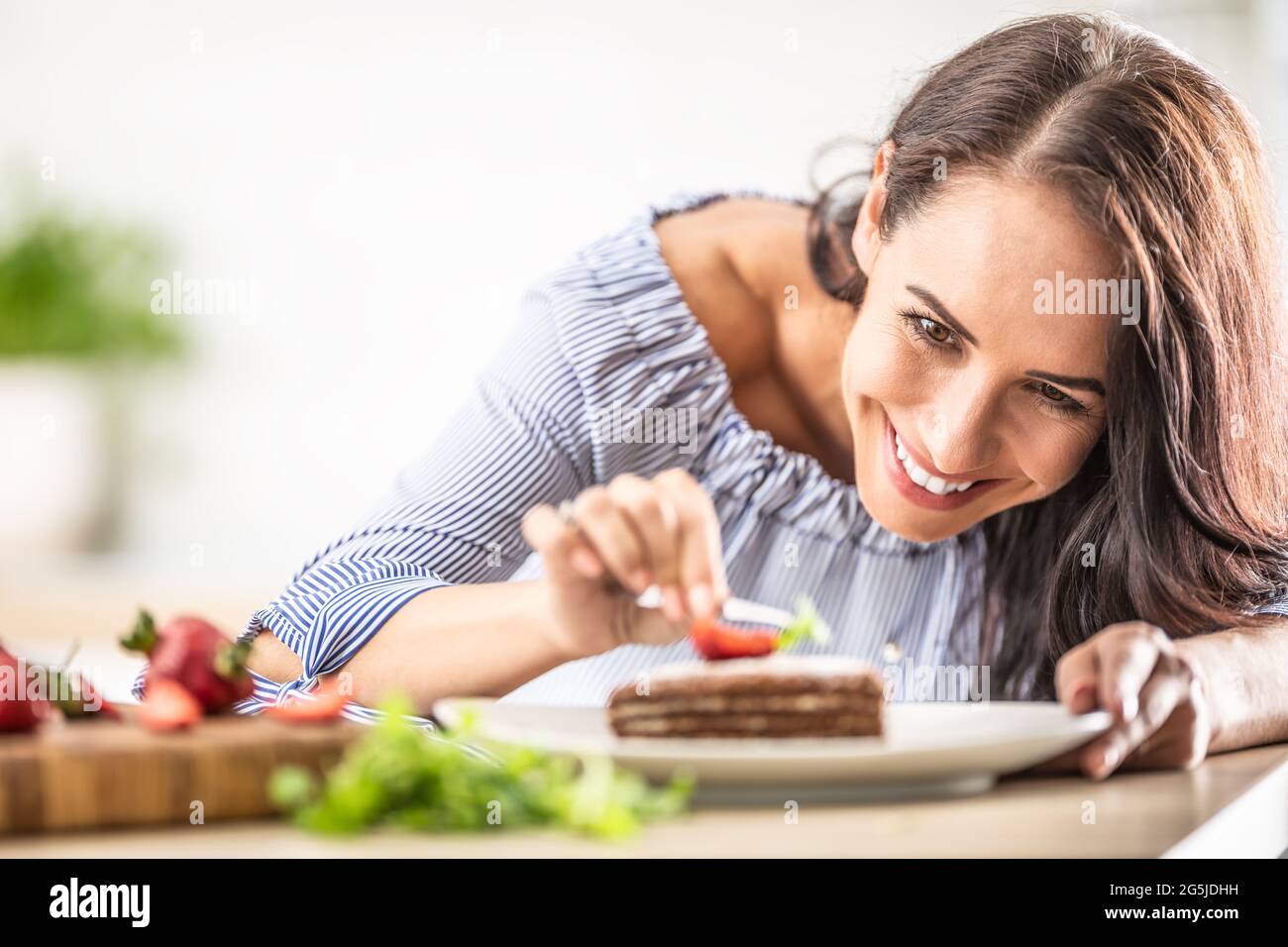 Lächelnde Frau schmückt fertigen Kuchen mit einer Pinzette. Stockfoto