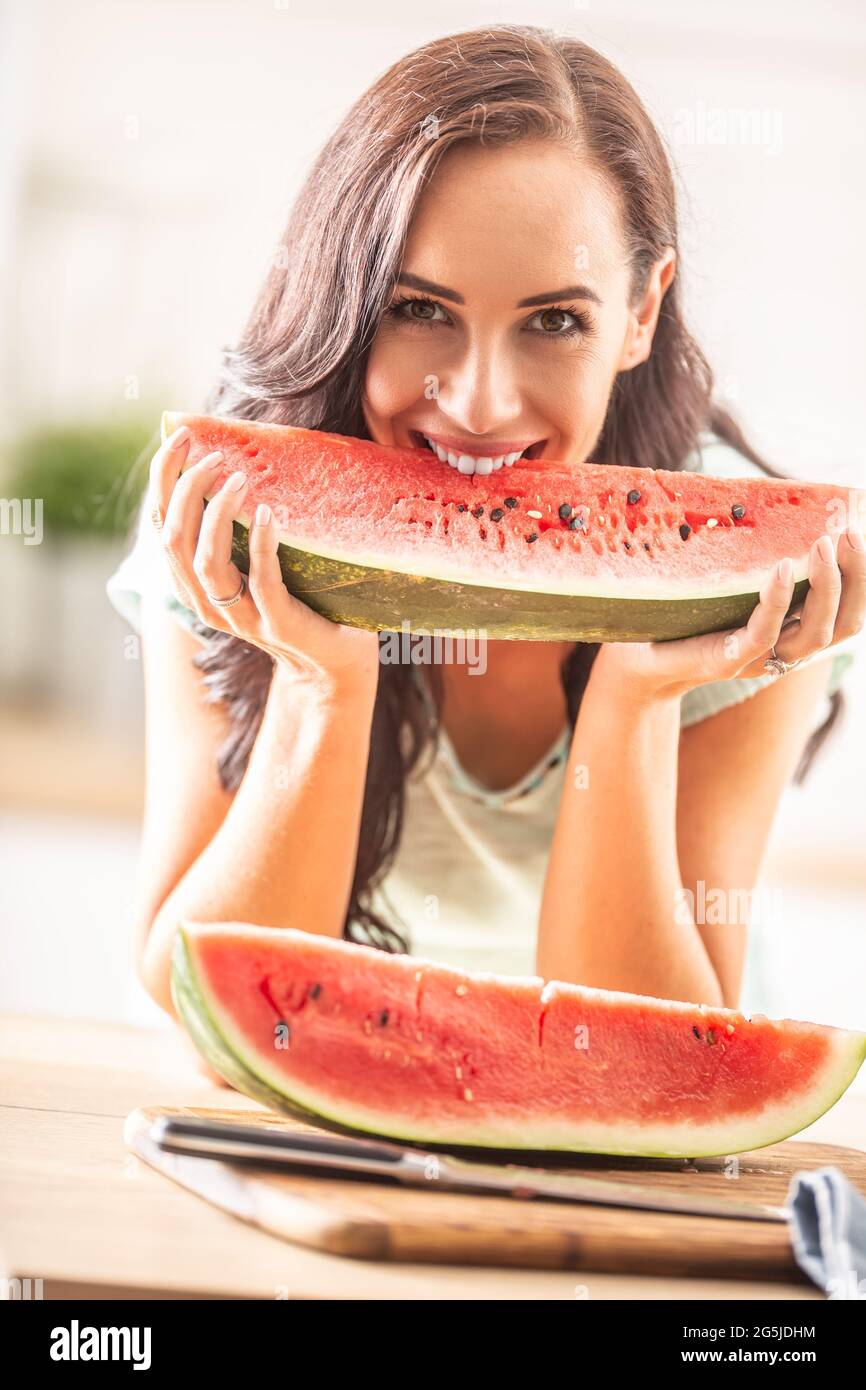 Gut aussehendes Mädchen beißt lächelnd in das Viertel einer Wassermelone in der Küche. Stockfoto
