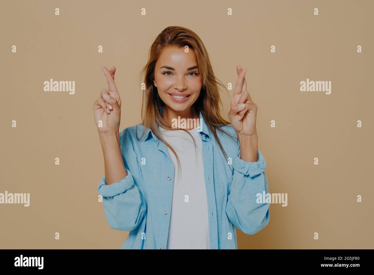 Positive Dame mit gekreuzten Daumen auf beigem Hintergrund Stockfoto